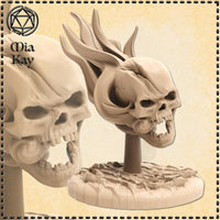 Digital render of an unpainted Flameskull miniature by Mia Kay M3DM, showing a snarling skull with swept-back flame crests and a prominent fang, mounted on a textured broken-stone base at 32mm scale — two angles displayed side by side