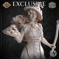 Close-up bust view of the unpainted white Dessert Witch miniature by Mia Kay M3DM, highlighting her knowing half-smile, wide curling witch hat with pastry charms, donut brooch necklace, ruffled neckline, and the detailed plate of stacked iced biscuits she holds aloft