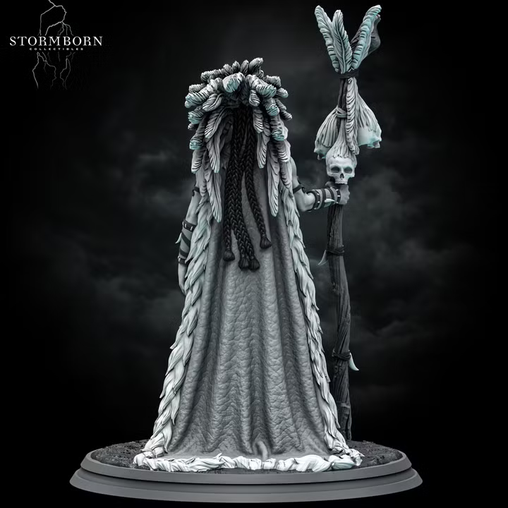 Orc shaman gripping a bone staff topped with skulls, feathered headdress framing a bird-skull mask, fur-and-feather mantle trailing to the ground. Figure on a round scenic base. Stormborn Collectibles.