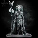 Orc shaman standing tall, holding a gnarled skull-topped staff, wearing a bird-skull headdress with sweeping feathers and a fur wrap with an animal skull at the waist. Sculpt by Stormborn Collectibles.