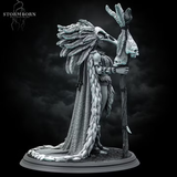 Orc shaman miniature with a towering feathered headdress and bone staff, wearing a fur-trimmed wrap and skull ornaments, standing on a textured scenic base. Sculpted by Stormborn Collectibles.